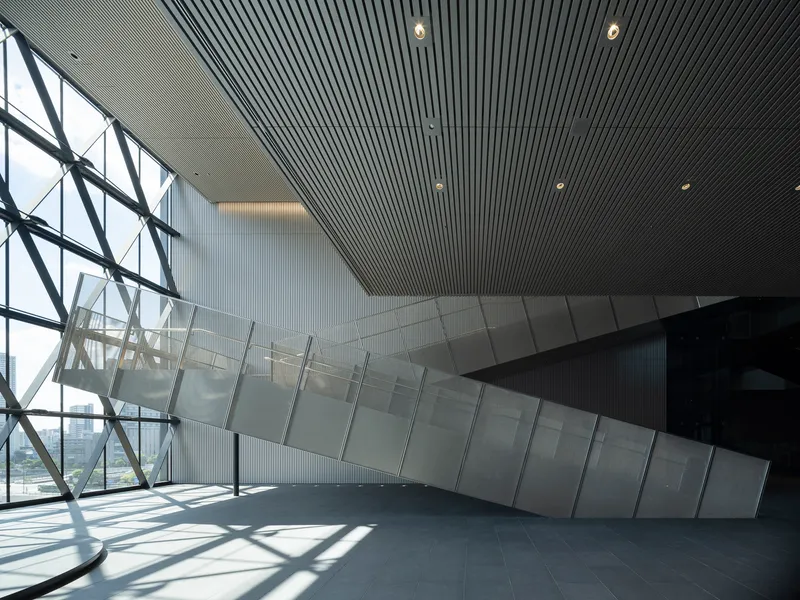 Diagonal steel bracing meets glass and ribbed ceiling panels with sunlight casting sharp shadows across the floor