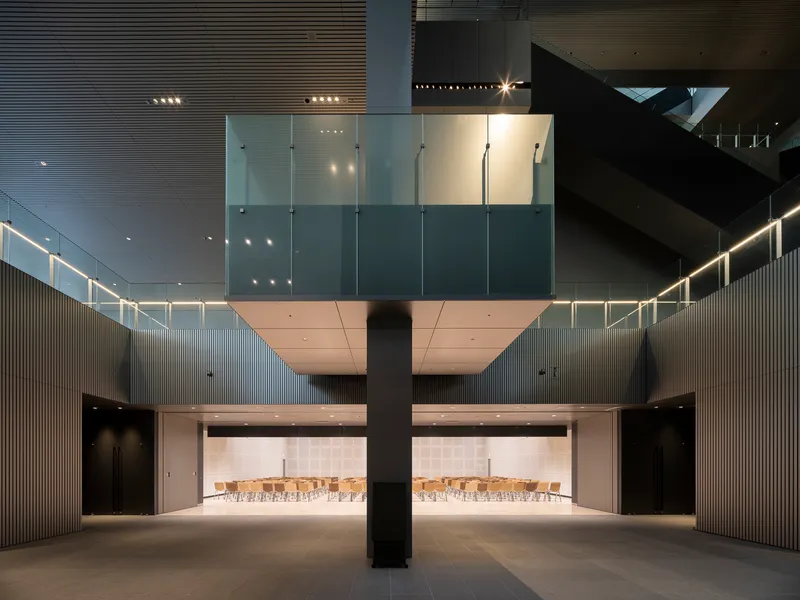 Interior lobby with central column, suspended volumes, and ribbed wall panels lit at dusk