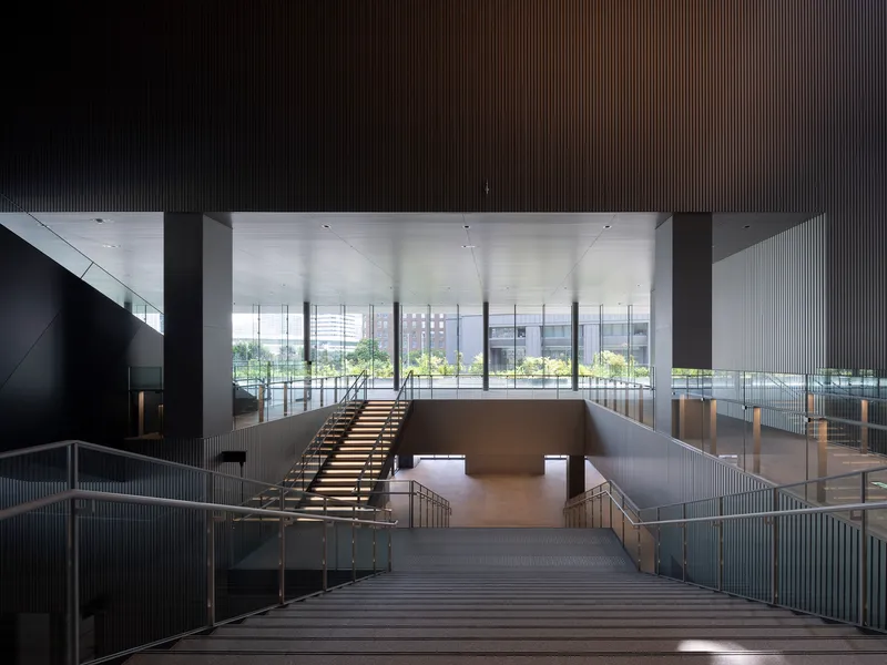 Central timber staircase descending toward perimeter glazing with park greenery visible beyond