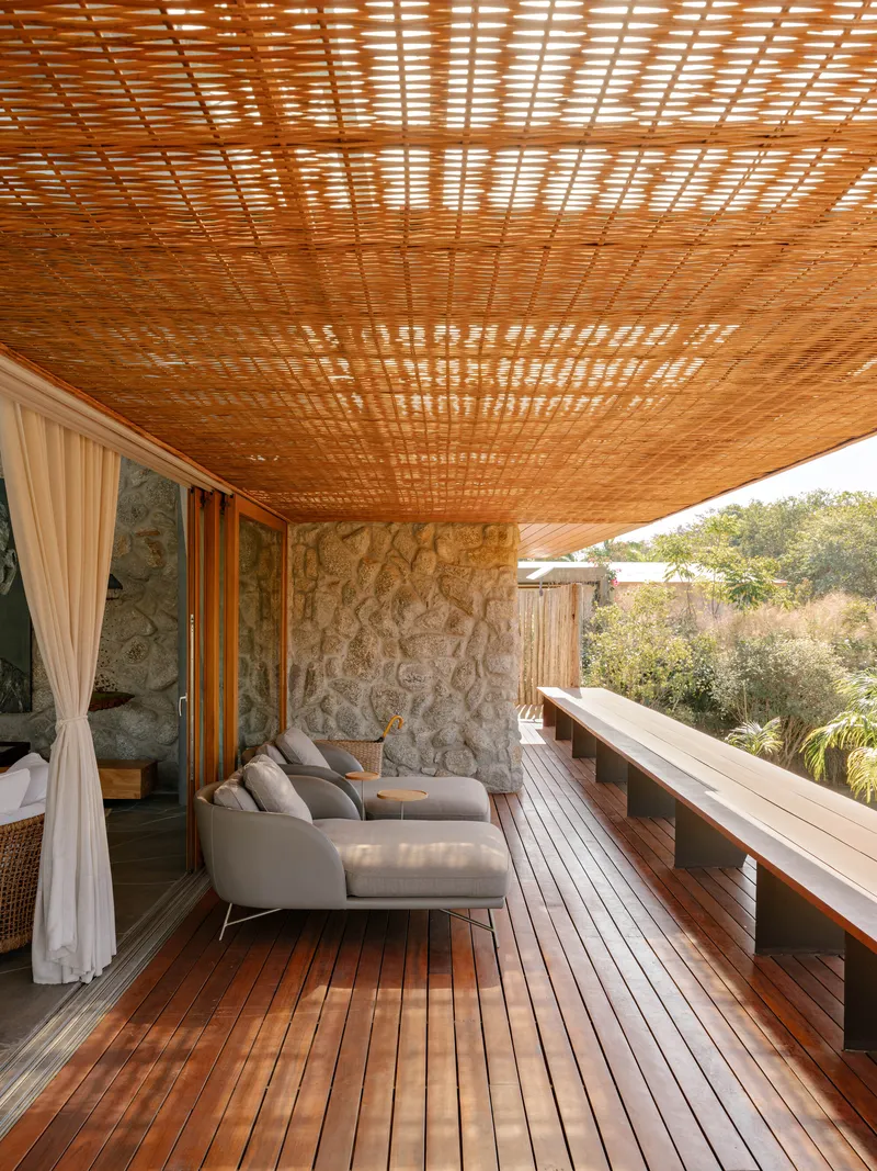 Covered deck with slatted timber ceiling casting dappled shadows over stone wall and timber flooring