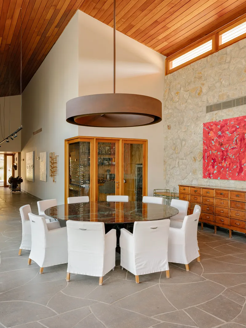 Dining area with circular drum pendant light above round table beneath vaulted timber ceiling and clerestory windows