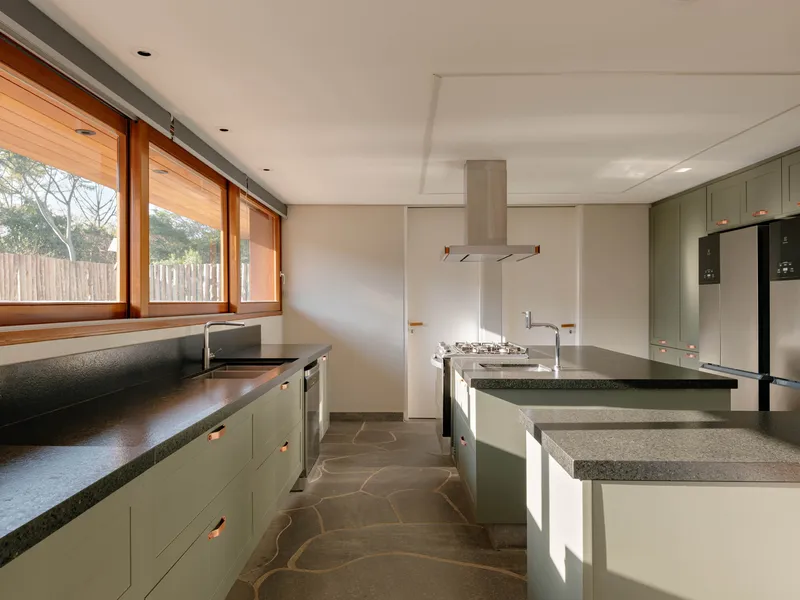 Kitchen with sage green cabinetry, dark stone countertops and irregular stone floor tiles in afternoon light