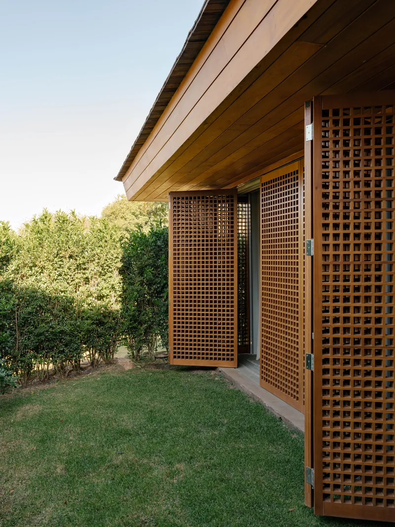Exterior view of timber lattice screen doors opening onto lawn with timber soffit and dense hedge beyond