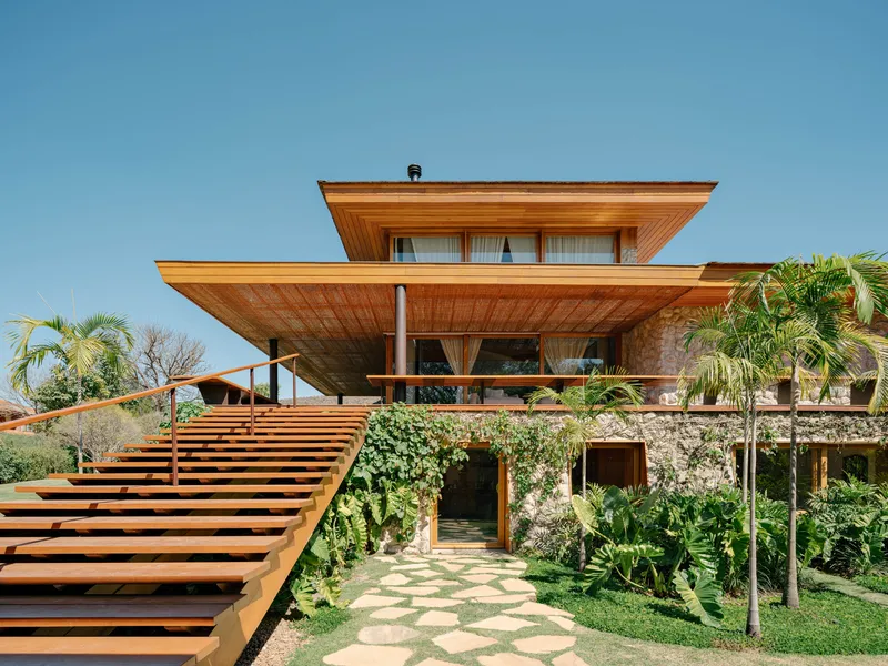 Garden facade with horizontal wood louvers and a stepped wooden entry stair flanked by palms