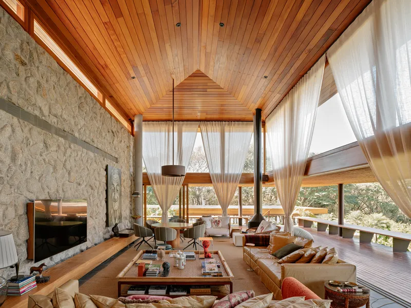 Double-height living room with stone fireplace wall and wood slat ceiling under sheer curtains