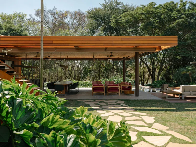 Covered outdoor terrace with exposed timber beams and stone paver pathways through planted beds