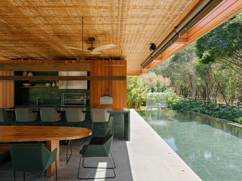 Open-air dining area with woven bamboo ceiling and timber clad kitchen wall beside reflecting pool