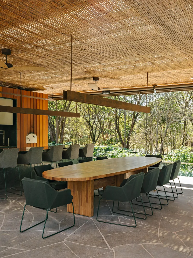 Long dining table under woven ceiling with timber beams and dappled sunlight filtering through trees