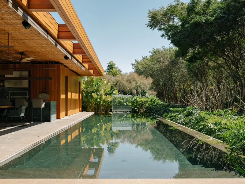 Linear reflecting pool bordered by stone pavers and planted beds beneath overhanging timber roof eaves