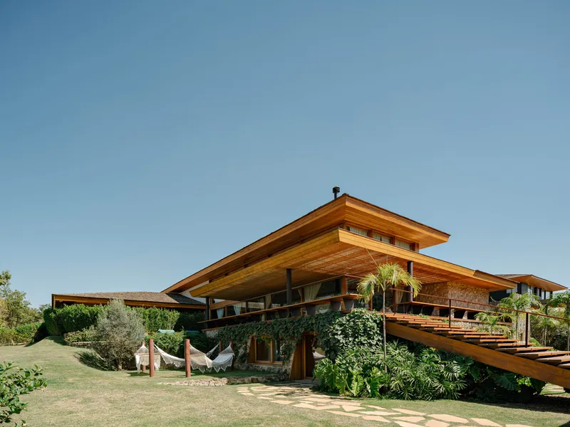 Garden elevation showing overhanging timber roofs, exposed rafters, planted terraces and hammocks on lawn in clear weather