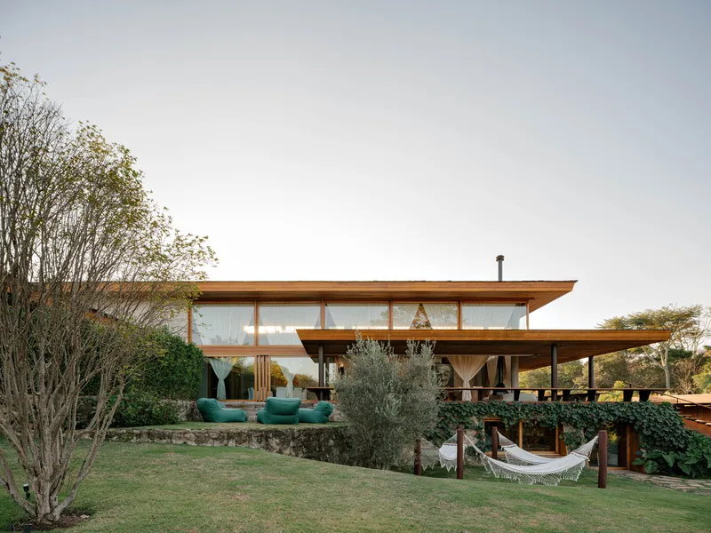 Garden view of the two-story timber residence with exposed beams and continuous glazing under overhanging roofs