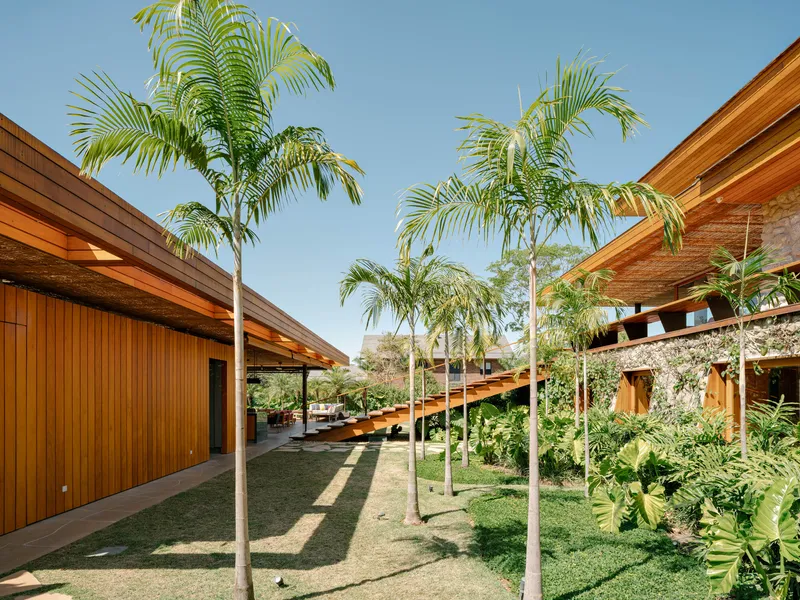 Courtyard with palm trees connecting the timber-clad volumes beneath sloped wooden roofs and exposed stone walls