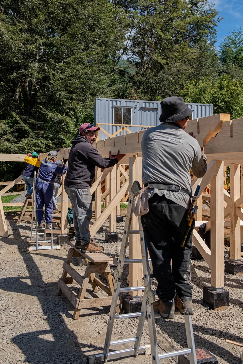 Three workers assembling timber frame structure on sawhorses under bright sunlight