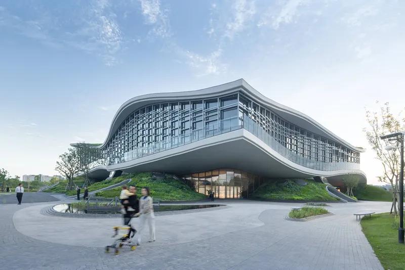 Entrance plaza with a curved water feature and pedestrians approaching the glass-walled facade on a clear day