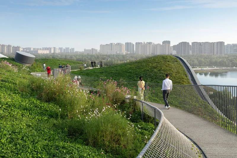 Rooftop walking path with planted meadow beds and metal railing overlooking the lake with distant towers