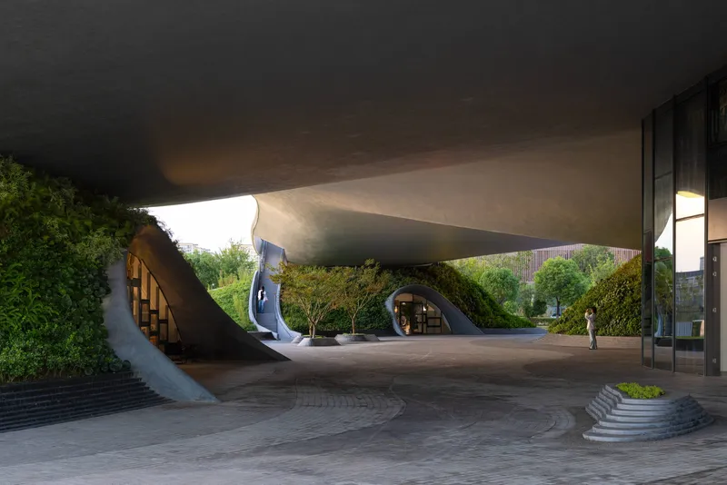 Covered forecourt beneath the concrete shell roof with curved stairs ascending to the planted roof