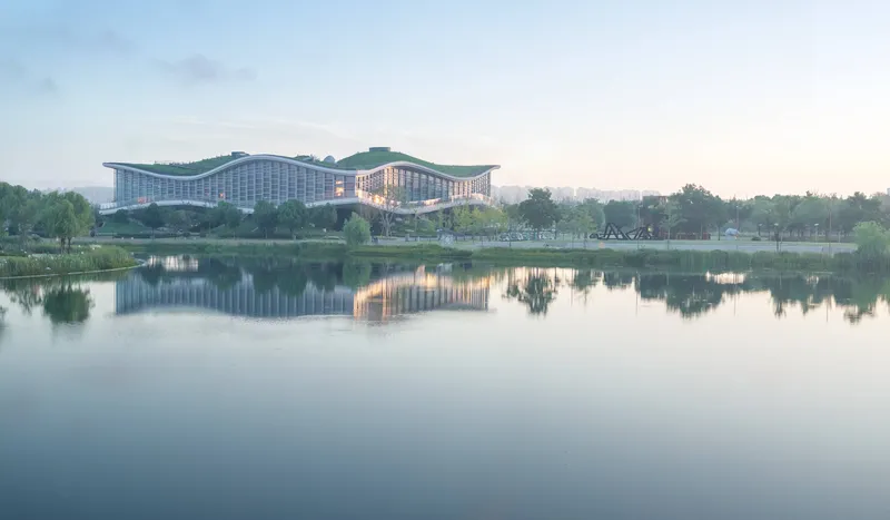 View across the lake showing the undulating green roof reflecting in still water at dawn