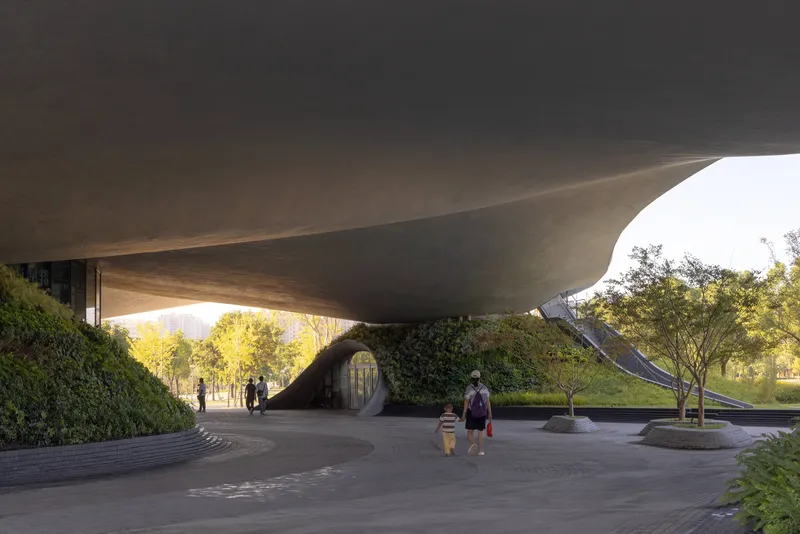 Visitors walking beneath the curved concrete underside of the elevated structure in afternoon light