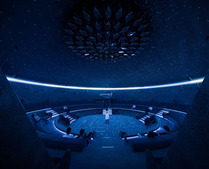 Circular planetarium interior with tiered seating beneath a crystalline geometric ceiling under a starry projection