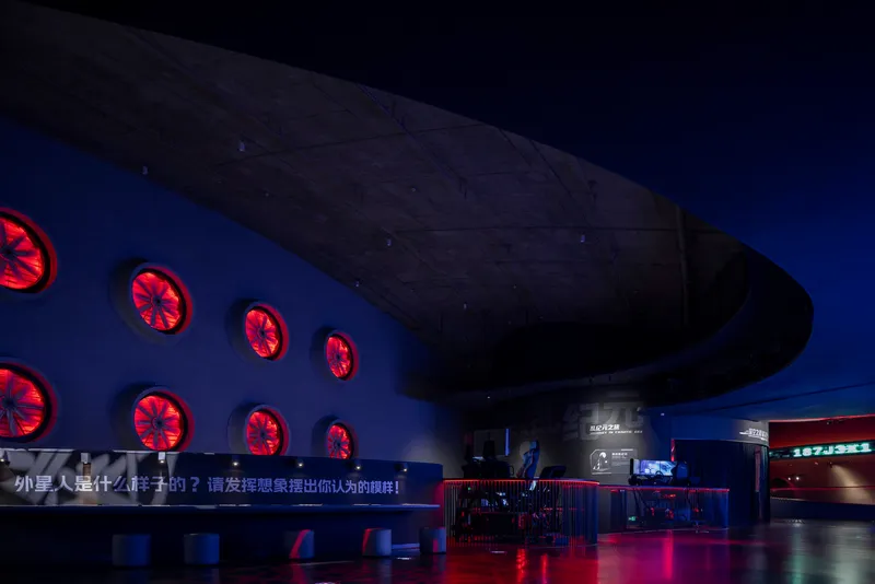 Interior exhibition hall with curved soffit and red illuminated circular ventilation grilles at twilight