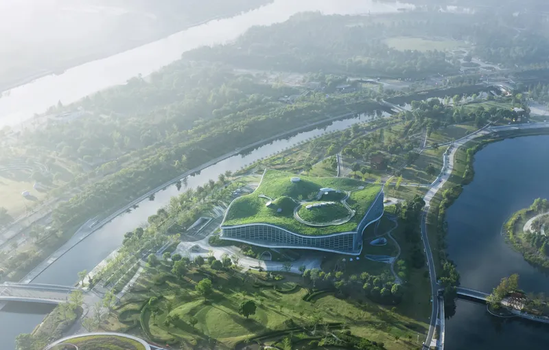 Aerial view of the curving building nestled in a landscaped peninsula between two rivers in morning mist