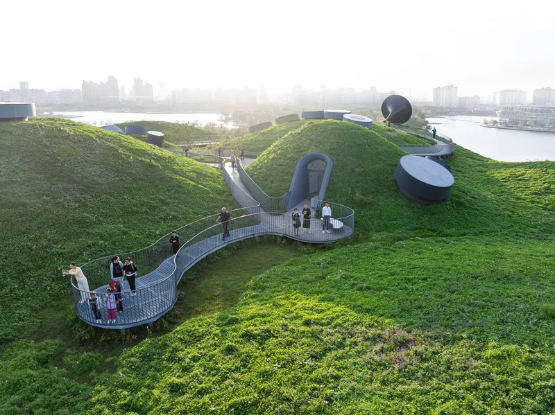 Steel mesh walkway winding across the planted green roof with visitors gathered on viewing platforms at dusk