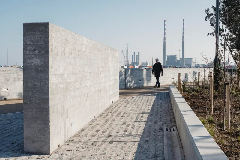 Cobblestone pathway along concrete parapet wall with pedestrian and industrial stacks in distance