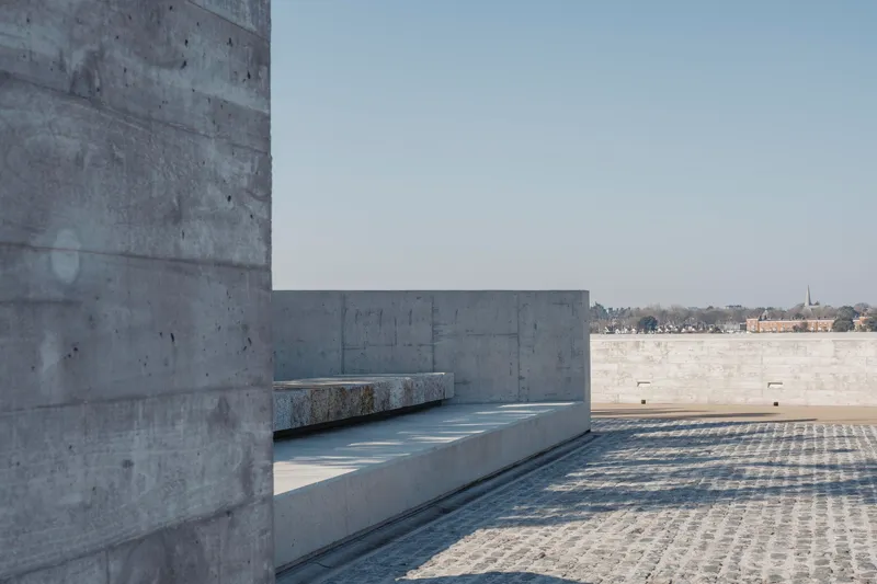Granite bench built into curved concrete wall overlooking cobblestone plaza and distant shoreline