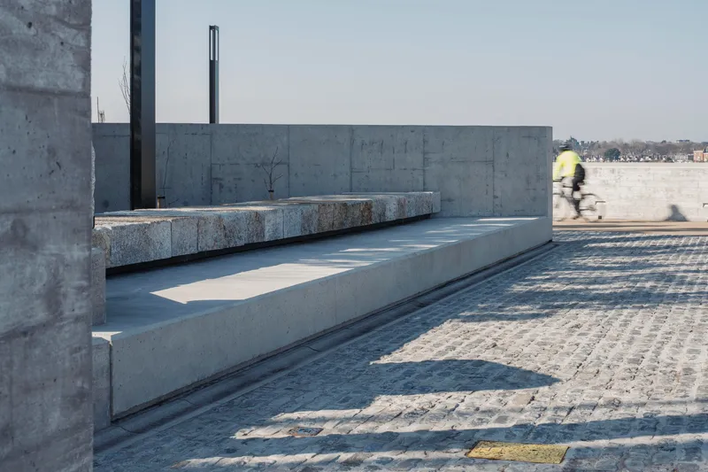 Cyclist in motion blur passing granite bench set into concrete terrace with metal posts