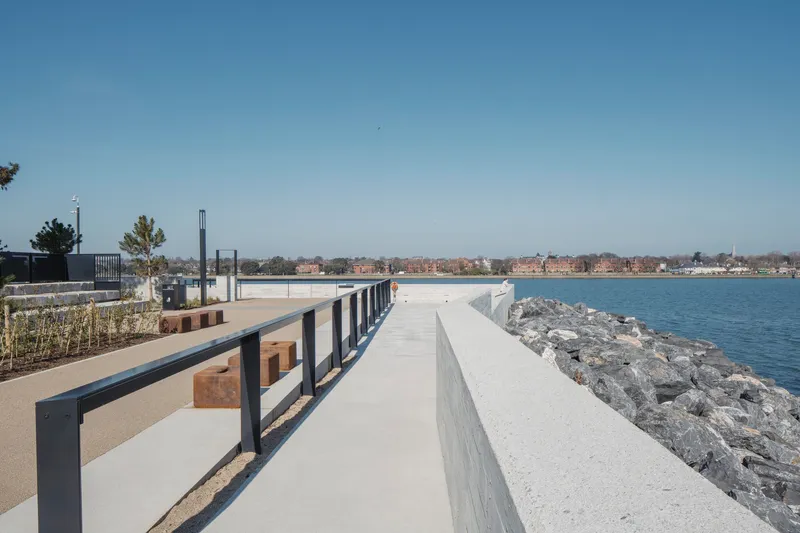 Waterfront promenade with timber benches between concrete walls and rocky shoreline