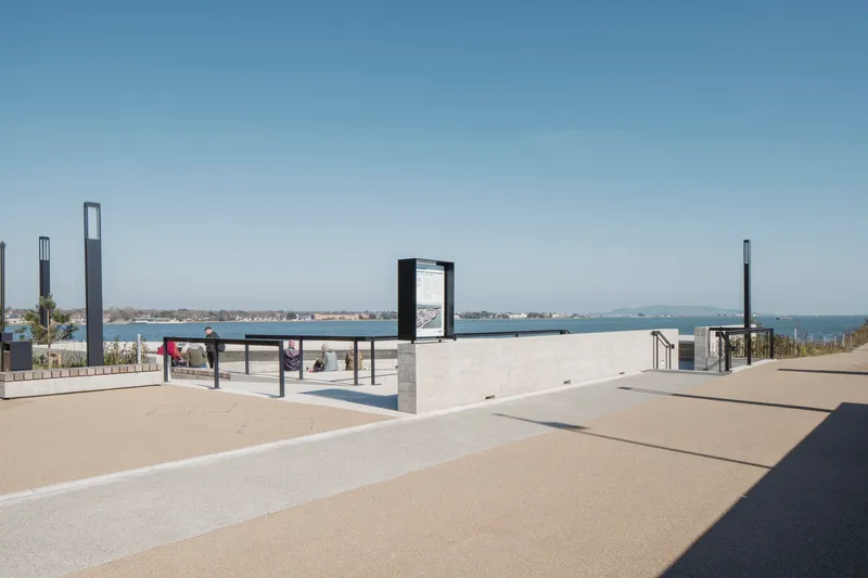 Paved plaza with information kiosks and concrete walls opening to views of the harbor
