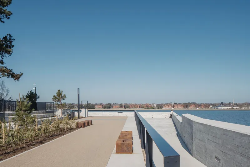 Boardwalk terrace with concrete walls and timber benches overlooking the waterfront under a clear blue sky