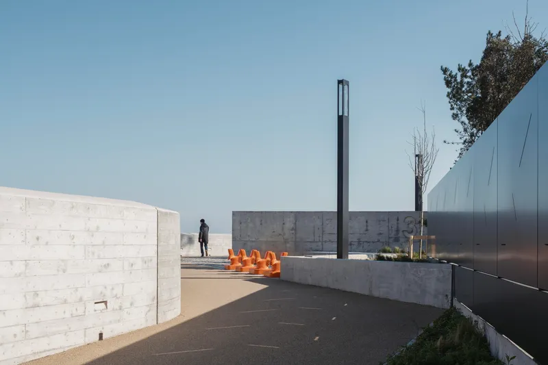 Plaza with concrete walls, tall black metal light post, and orange sculptural elements on a planter