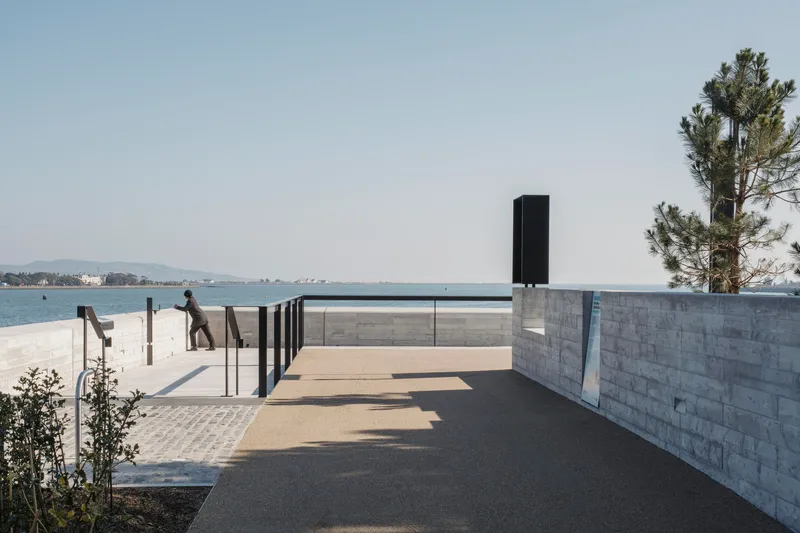 Waterfront promenade with concrete retaining walls, metal railings, and dog sculptures on the sand