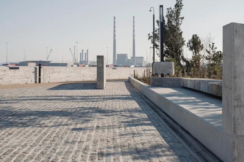 Granite block paving and concrete benches overlooking industrial harbor infrastructure in the distance
