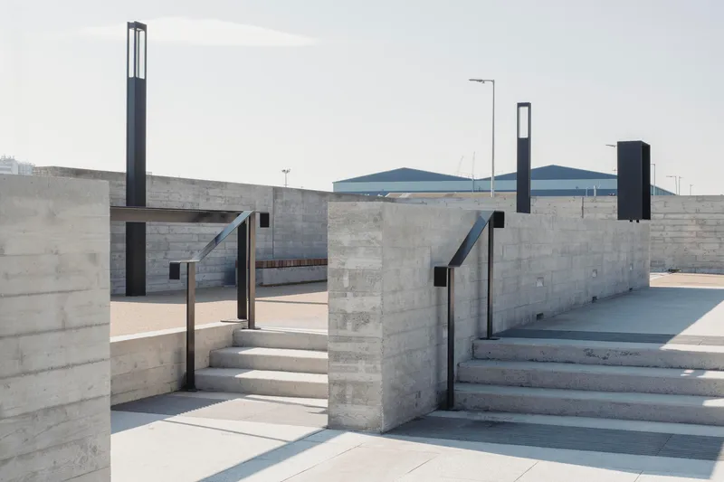 Concrete staircases descending between perpendicular walls with black metal railings under overcast sky