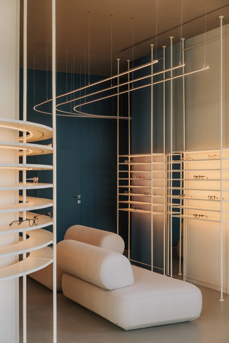 Interior corner showing curved suspended lighting and vertical brass rods framing eyewear displays against a deep teal wall
