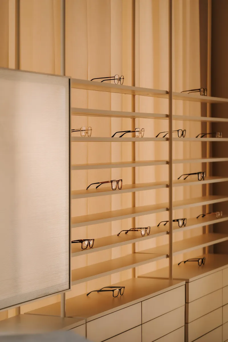 Brass shelving system with eyeglasses mounted against backlit translucent wall panels