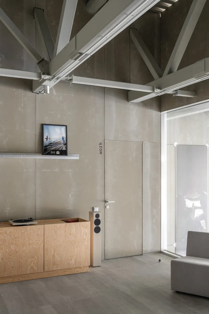Flush concrete wall panels with recessed door, pale wood credenza, and exposed ceiling trusses