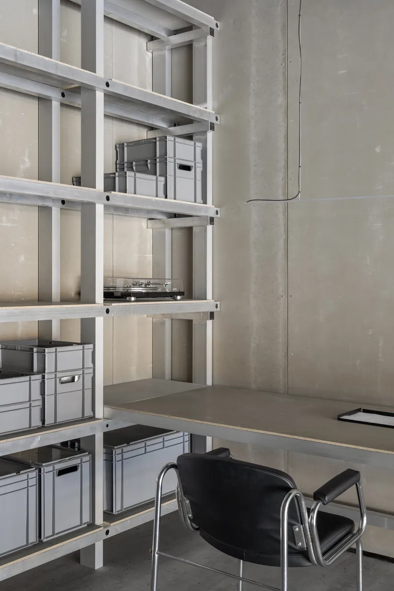 Cantilevered desk with open aluminum shelving holding grey storage boxes against concrete panels