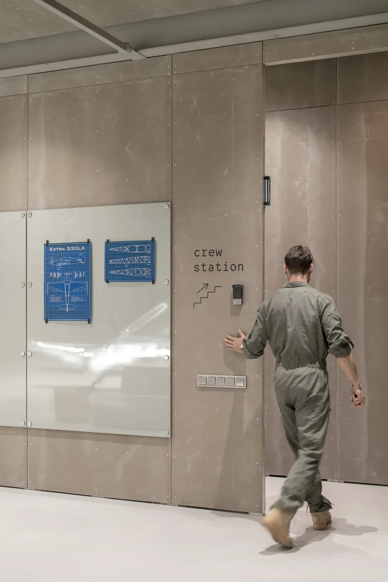 Person approaching concrete wall with mounted blueprints and signage near a recessed doorway