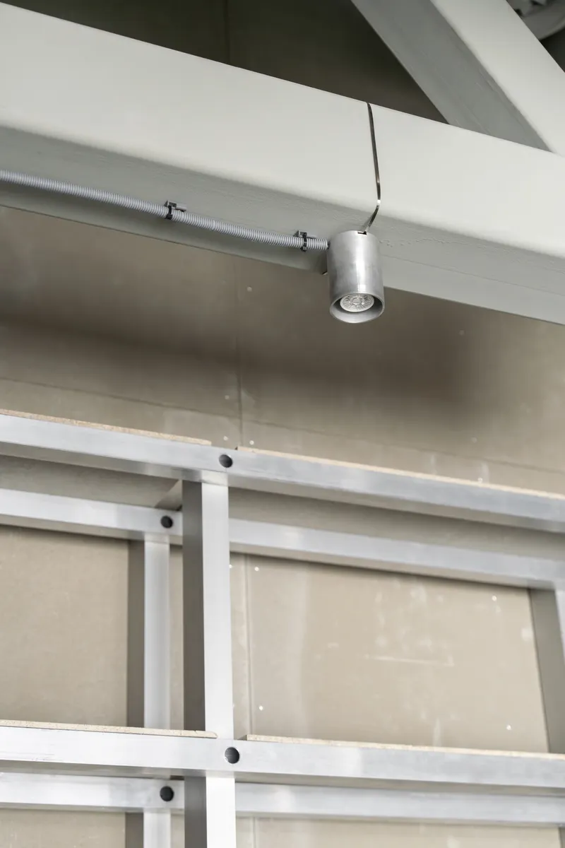 Ceiling detail showing exposed conduit, cylindrical spotlight fixture, and white painted steel structural frame