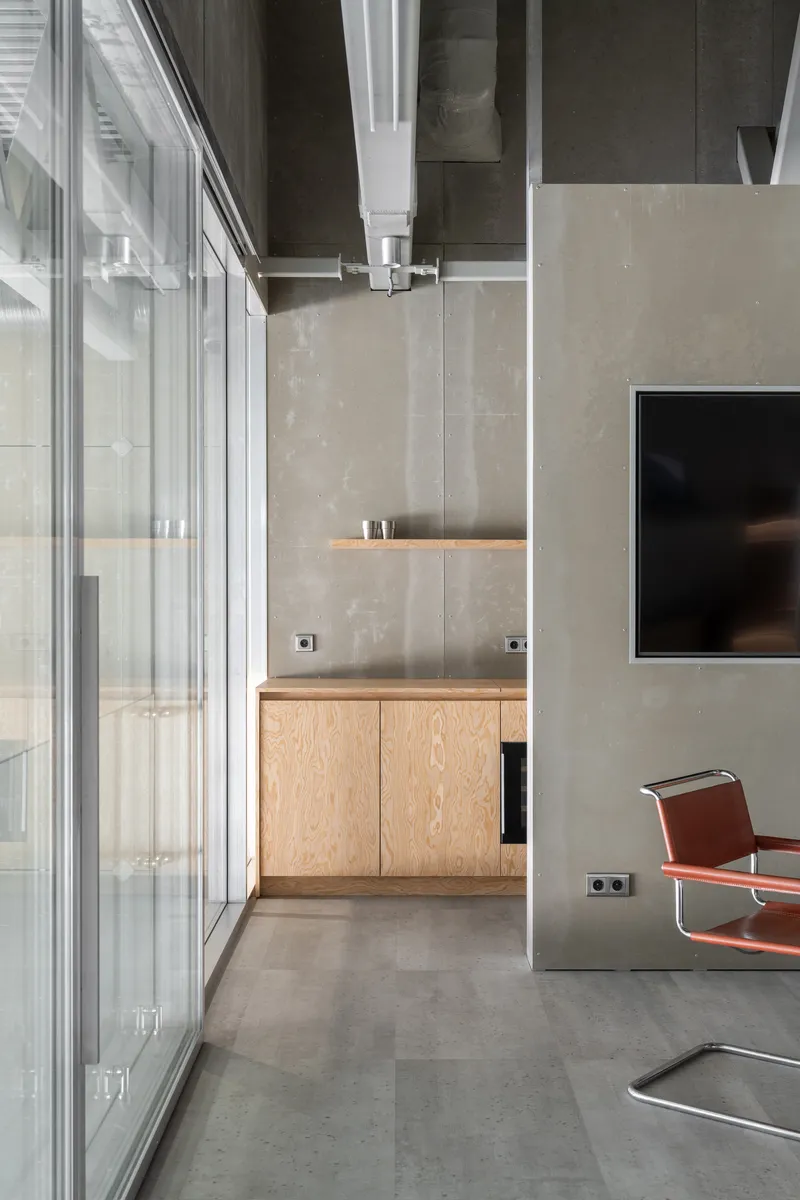 Corner with floor-to-ceiling glazing, plywood cabinetry, and concrete column beside partial view of red chair