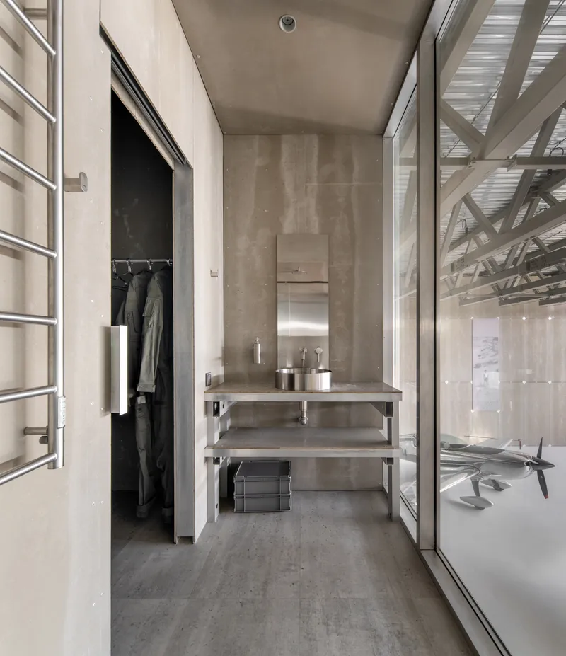 Bathroom corridor with concrete walls, steel frame vanity, recessed closet, and glazed wall revealing hangar beyond