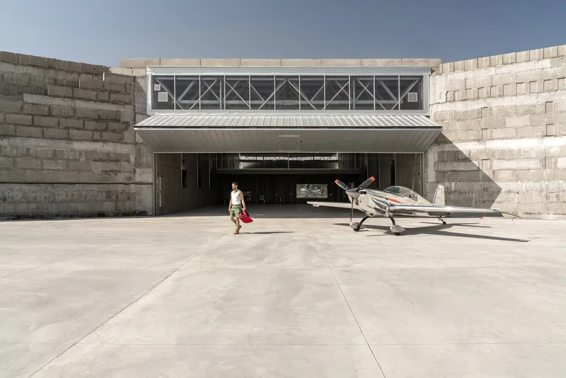 Concrete hangar entrance with stepped retaining walls and figure walking toward parked aircraft on paved apron