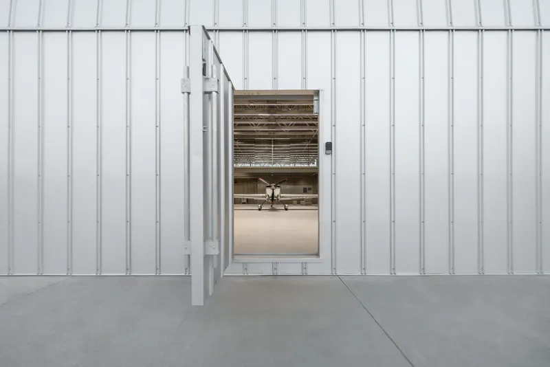 Corrugated metal cladding wall with open sliding door revealing aircraft inside the hangar bay