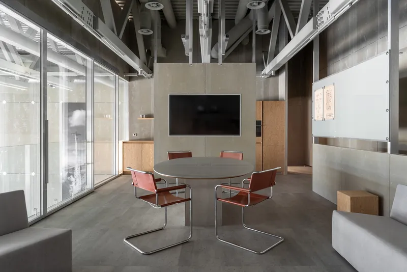 Conference room with exposed ceiling structure, round table, red cantilever chairs, and floor-to-ceiling glazing