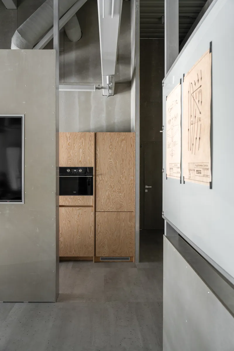 Kitchenette with pale wood veneer cabinetry, built-in oven, and exposed structural beams overhead