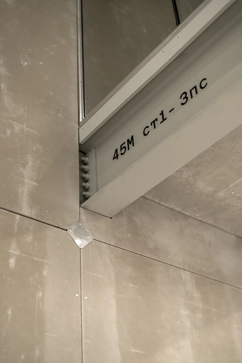 Close-up of white steel frame member with stenciled code marking against concrete panel joint