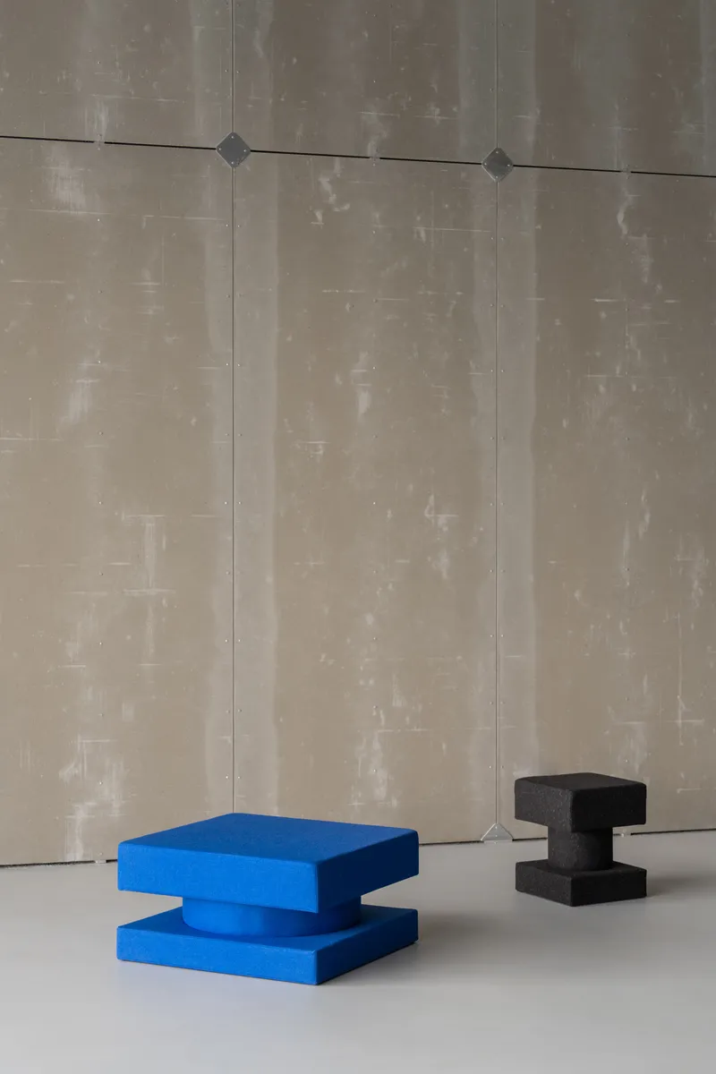 Blue and black sculptural seating blocks on a white floor against weathered concrete panel walls